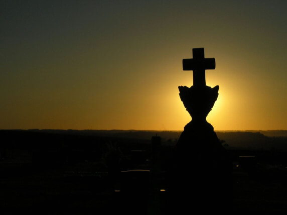 A cross is silhouetted against the setting sun.