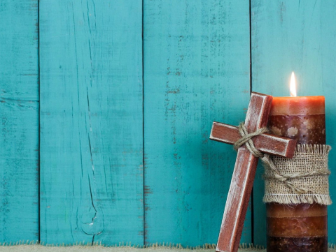 A cross and candle on the ground in front of a blue wall.